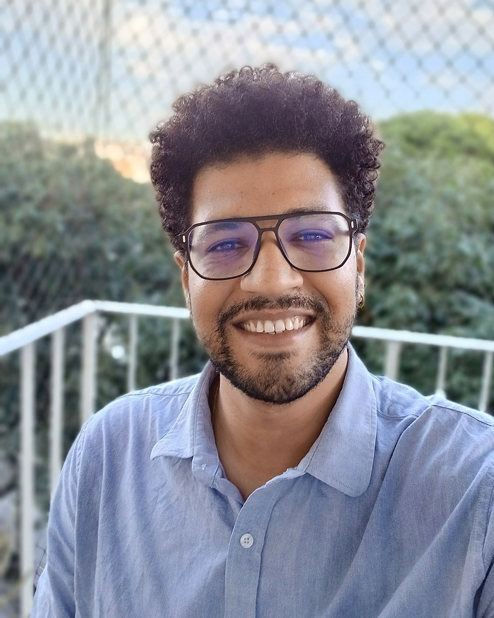 Retrato do autor, Alan Cristian Valentim, em camisa social azul, sorrindo